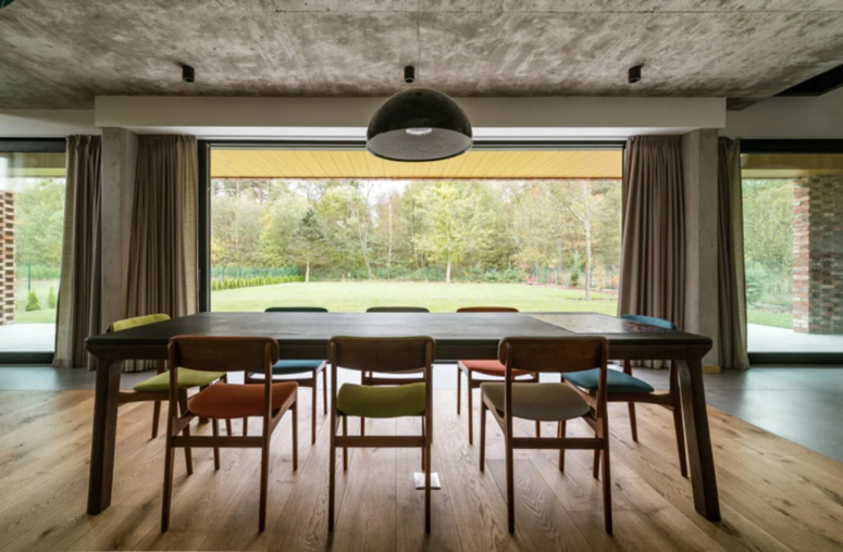 The dining space is placed in front of the window, with colorful chairs and a concrete ceiling that contrasts the warm decor The dining space is placed in front of the window, with colorful chairs and a concrete ceiling that contrasts the warm decor