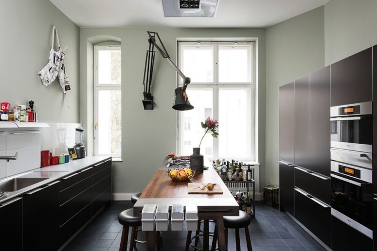 The kitchen is done with black sleek cabinets, with a statement wall lamp and a cool dining table