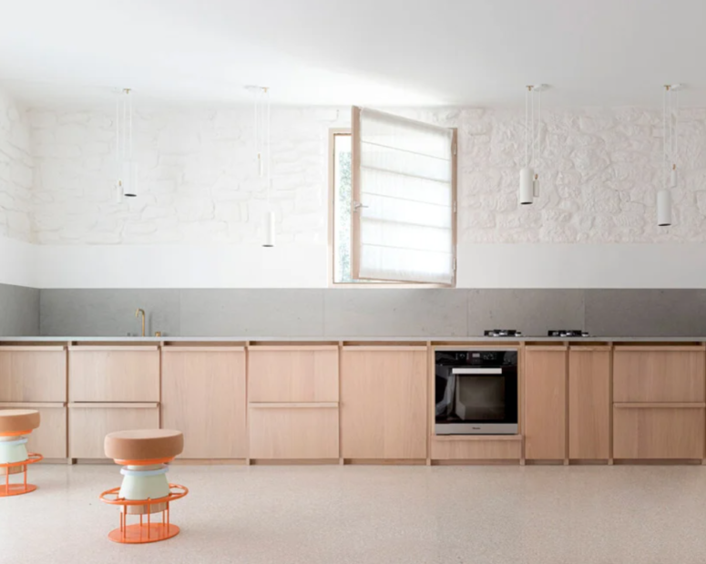 The kitchen is done with white walls, a grey backsplash, sleek plywood cabinets and white pendant lamps