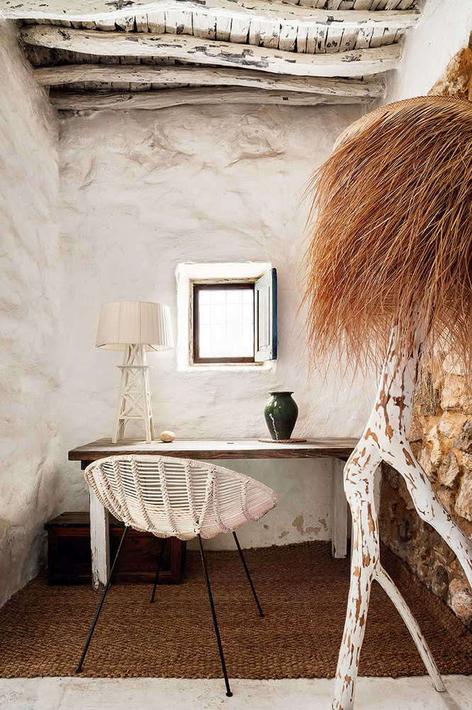 The tiny home office is done with a shabby chic desk, a wooden box, a jute rug, some catchy decor and a green vase
