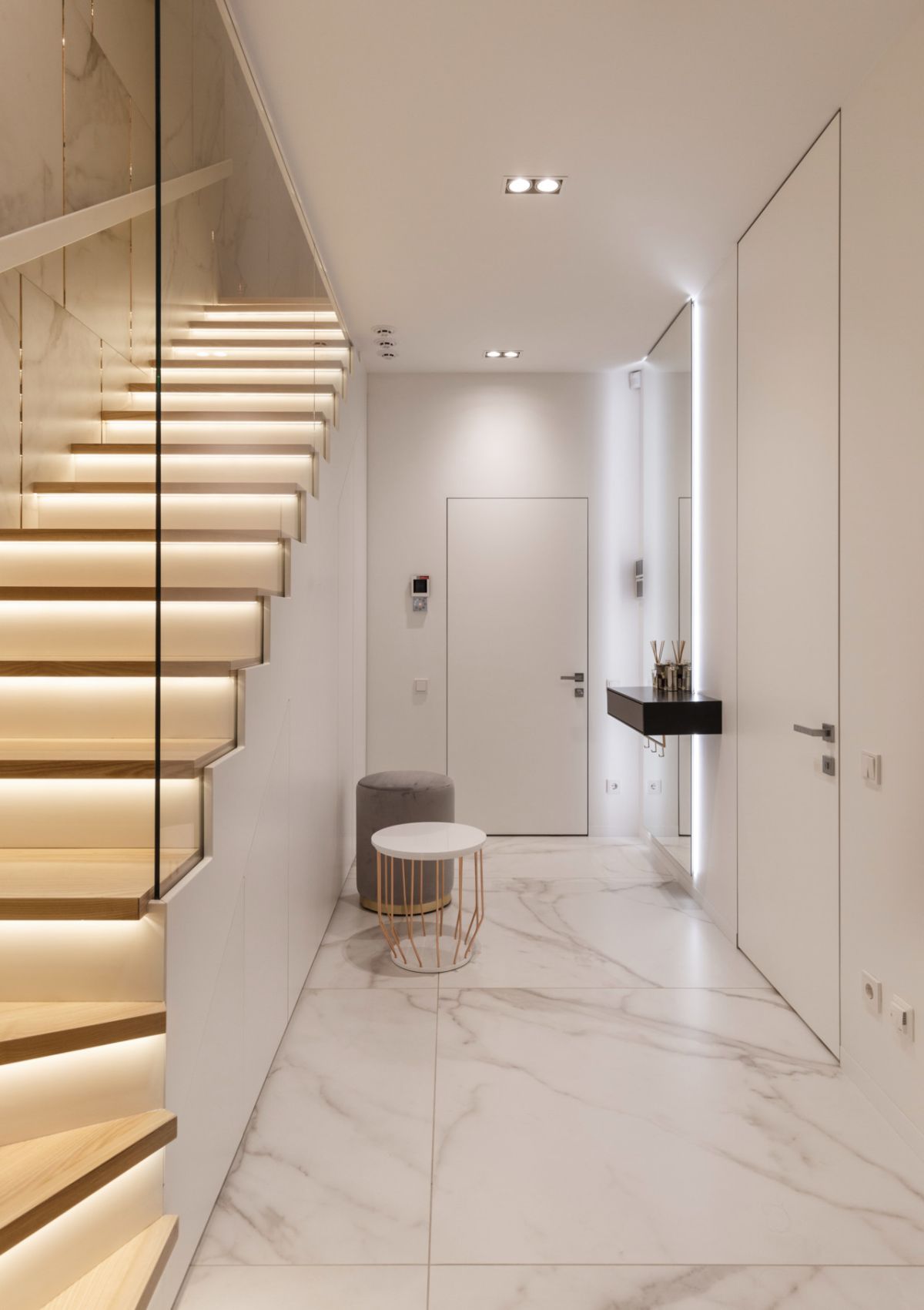 The entryway is very laconic, with white marble tiles and neutral stools and tables
