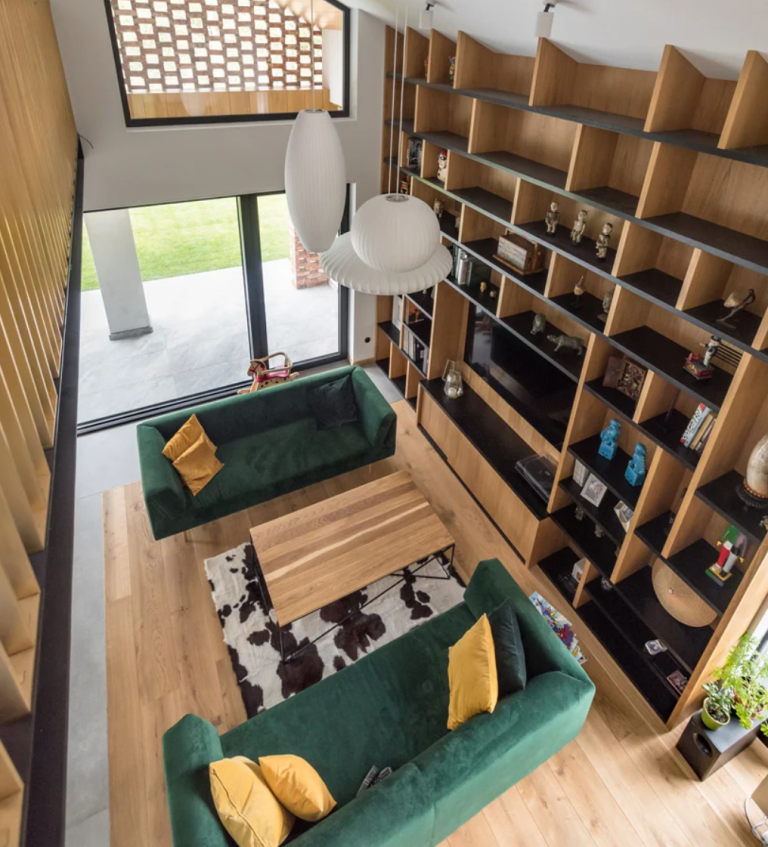 a homie library right in a living room The living room is done with bold green sofas, yellow pillows, a large bookcase that takes a whole wall