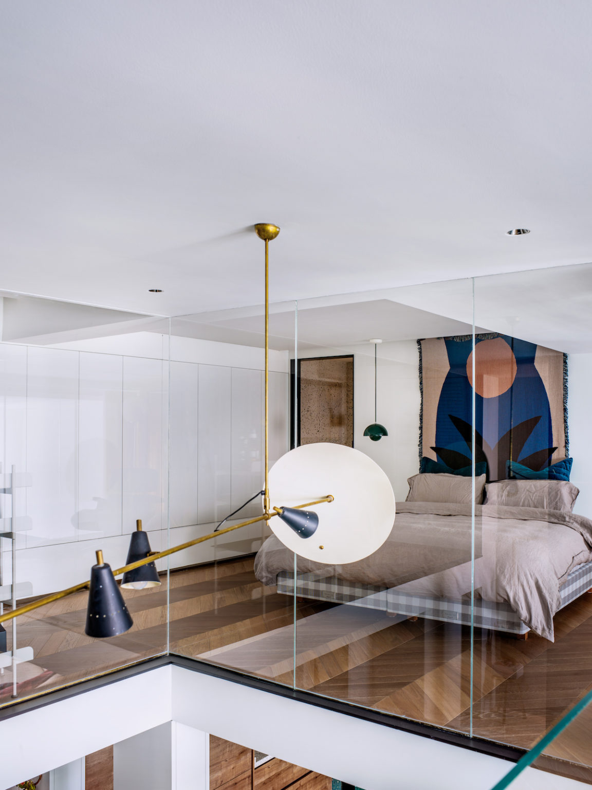 The bedroom features closed and sleek storage units, a floating bed, a bright artwork and hanging lamps