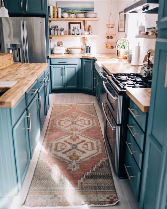 a beautiful kitchen in blue, with wooden countertops, white walls and a boho rug that refresh the space