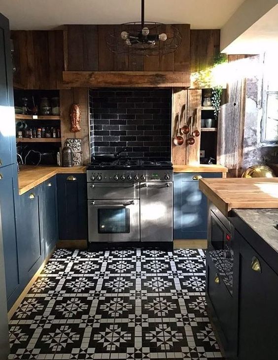 a blue kitchen with light-colored wooden countertops, a wooden hood and a dark tile backsplash plus a vintage lamp