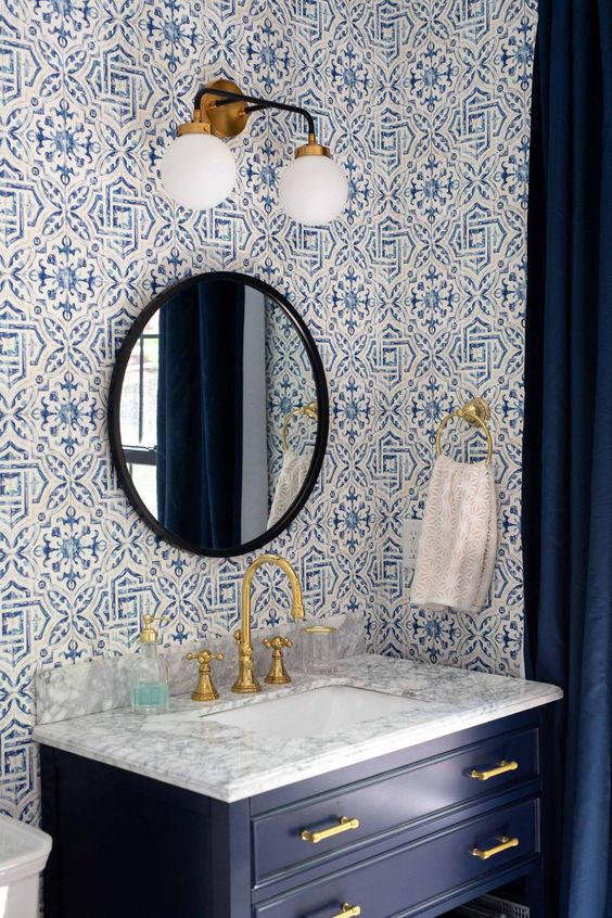 a bold powder room with mosaic tiles on the walls, a navy vanity, a stone sink, a sconce and a black framed mirror