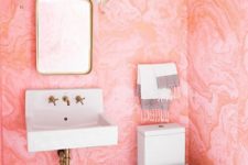 a bold powder room with pink watercolor wallpaper on the walls, black and white tiles and brass fixtures for more chic