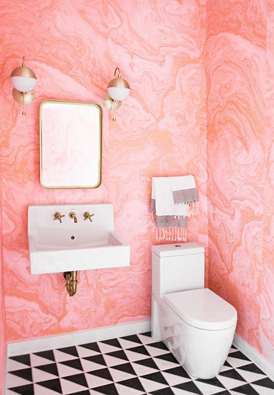 a bold powder room with pink watercolor wallpaper on the walls, black and white tiles and brass fixtures for more chic