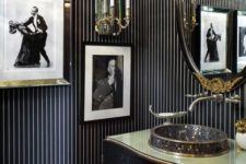 a bold vintage black and gold bathroom with an elegant vanity, a catchy sink, a refined mirror and bold artworks