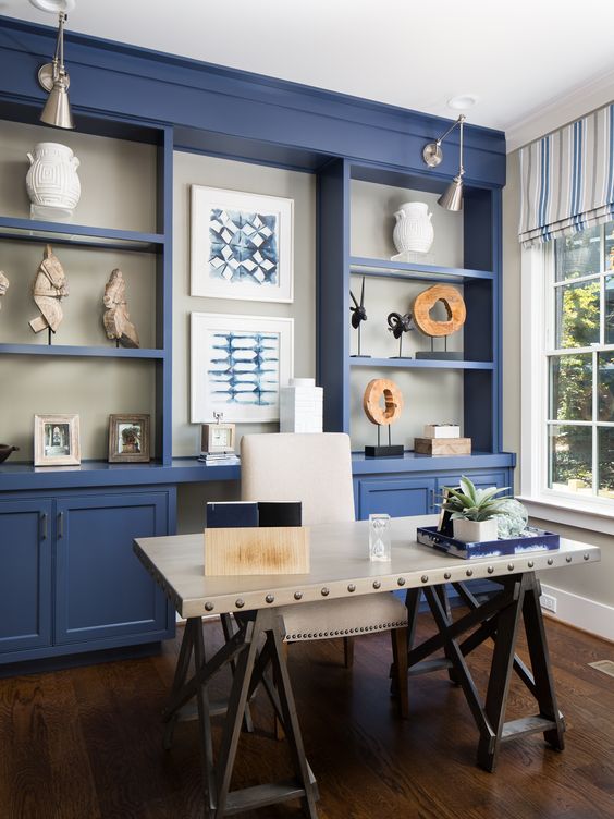 a bright blue home office with a large storage unit that takes a whole wall, a white industrial desk, a white chair and striped curtains