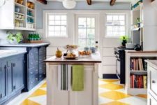 a bright kitchen with a geometric yellow and white floor, navy cabinets and dark stained wooden beams on the ceiling
