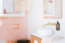 a catchy bathroom with pink tiles, a wicker lamp and basket, a floating vanity and gold fixtures for a glam touch