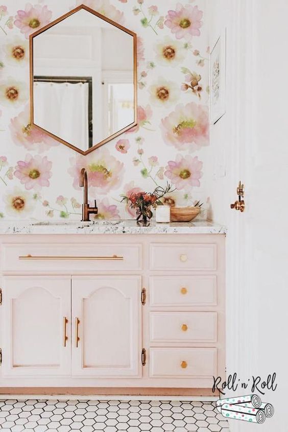 a chic and girlish bathroom with pink floral wallpaper, a light pink vanity and gold and copper fixtures and frames