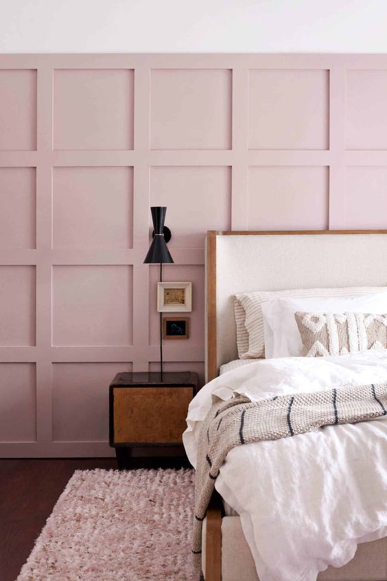 a chic bedroom with a pink paneled wall, a white bed, dark nightstands and sconces plus neutral embroidered bedding