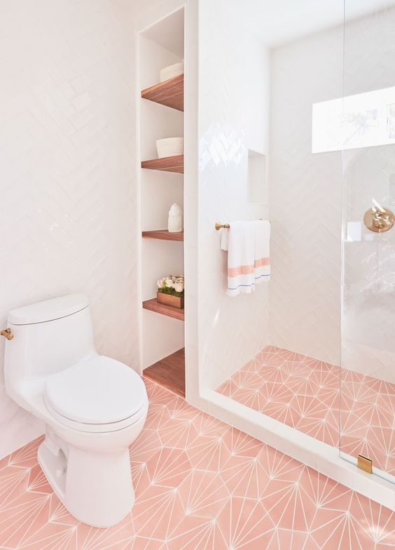 a chic contemporary bathroom with pink printed tiles on the floor, gold touches and fixtures plus simple white tiles on the walls