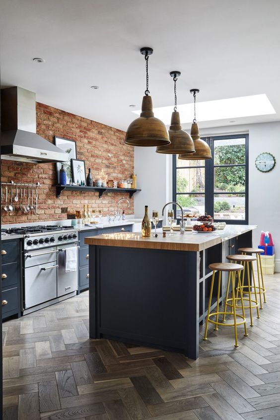 a chic navy kitchen with a brick wall, wooden countertops and metal lamps over the table for a bold look