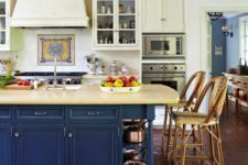 a chic traditional kitchen with light yellow walls, cabinets and a navy kitchen island plus tiles on the floor