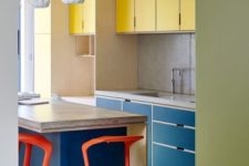 a colorful modern kitchen done in yellow and navy, with a stone countertop, red stools and a green floor is extra bold