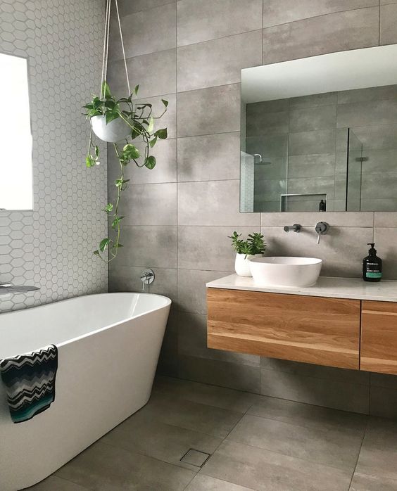 a concrete tile bathroom with an oval tub, a floating vanity, a mirror and some potted greenery is cool