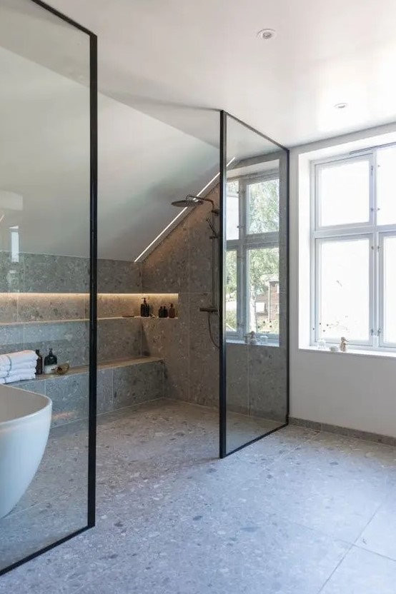 a contemporary attic bathroom clad with grey terrazzo tiles, a shower space, a lit up niche for storage, some windows