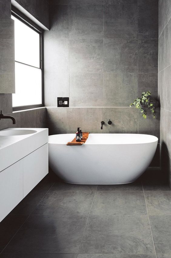 a contemporary grey bathroom clad with tiles, with a floating vanity and an oval tub plus greenery to refresh the space