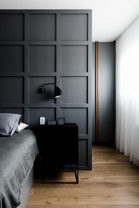 a contemporary mmoody bedroom with a statement graphite grey paneled wall that separates the sleeping space from the closet