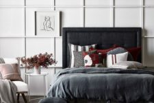 a contrasting bedroom with a white paneled wall, a blakc upholstered bed, dark bedding and a white chair looks ultra-modern