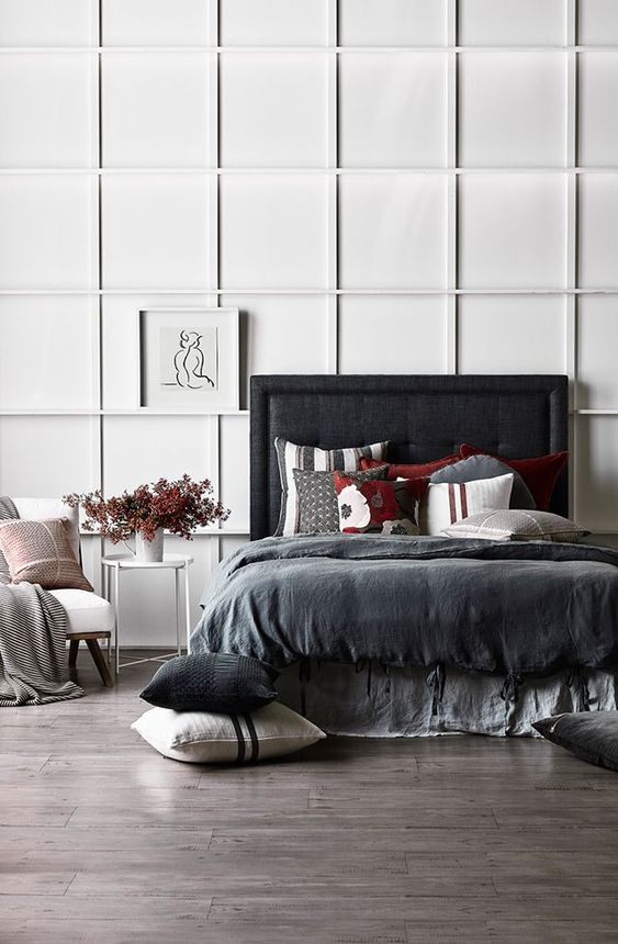 a contrasting bedroom with a white paneled wall, a blakc upholstered bed, dark bedding and a white chair looks ultra-modern