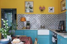 a cozy small kitchen with bright yellow walls and mosaic tiles on the backsplash, bright blue cabinets and vintage wall sconces