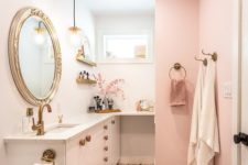 a cute glam bathroom with pink and white walls, pink towels, brass and gold fixtures and a refined mirror in a chic frame