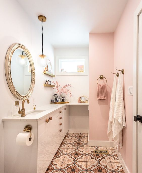 a cute glam bathroom with pink and white walls, pink towels, brass and gold fixtures and a refined mirror in a chic frame