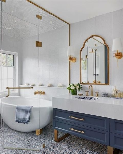 a floor clad with blue and white mosaic tiles, a blue vanity, gold fixtures, gold lamps and a bold printed sink