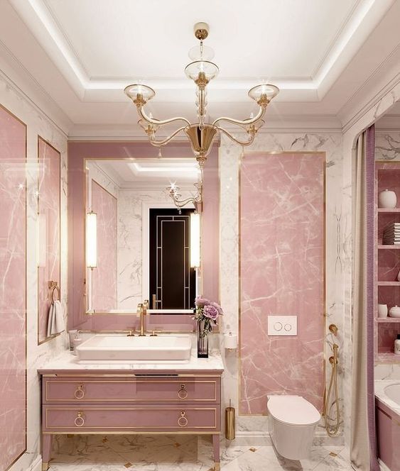 a glam pink bathroom done with stone and marble, with a refined pink vanity, a vintage chandelier and gold fixtures