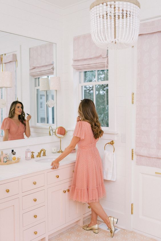 a glam vintage inspired pink bathroom with pink shades, pink tiles on the floor, a blush vanity and touches of gold here and there