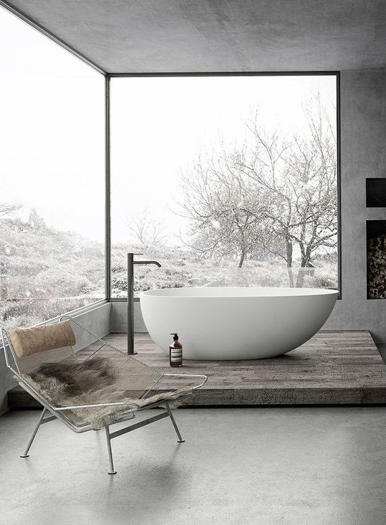 a gorgeous grey bathroom done with concrete, with glazed walls, a fireplace and a tub on a platform