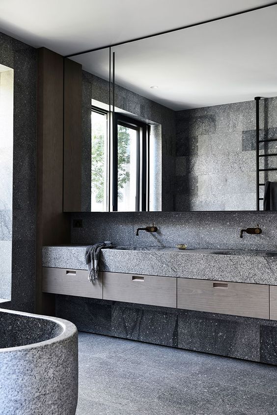 a gorgeous minimalist grey bathroom made of stone slabs, with an oversized mirror and a cool oval tub