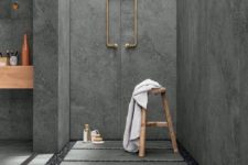 a grey concrete bathroom with pavement tiles and gravel on the floor plus gold fixtures to add chic to the space
