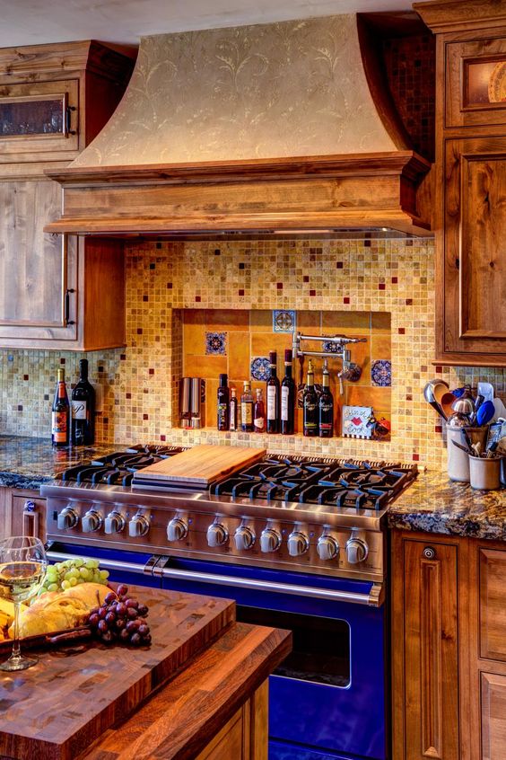 a light brown kitchen with a wood clad hood, a mosaic backsplash and a bright blue cooker is extra bold