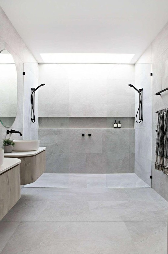 a minimalist bathroom clad with concrete, two floating vanities, round sinks, black fixtures and glass partitions