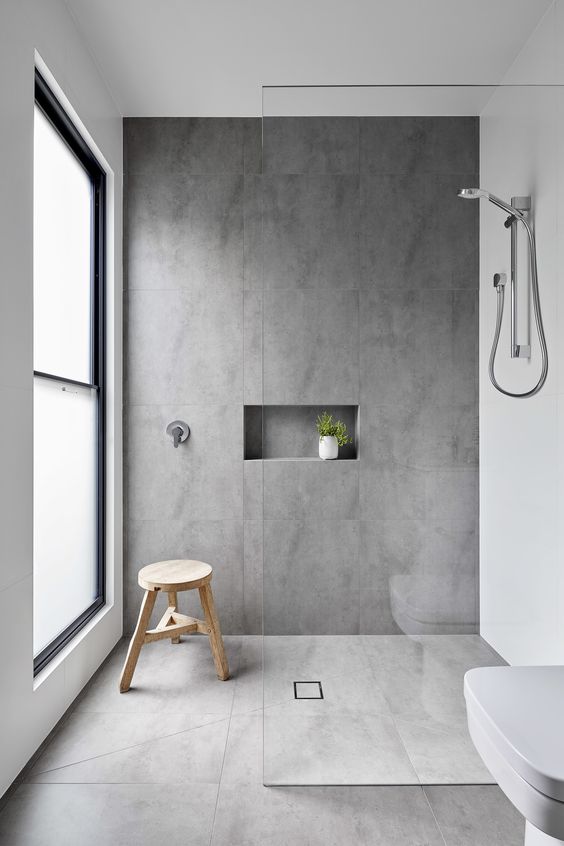 a minimalist bathroom clad with large scale tiles, a window with frosted flass, appliances and potted greenery