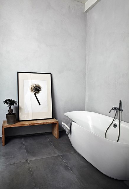 a minimalist bathroom with large scale tiles on the floor, an oval tub, a wooden bench and some decor is a beautiful space