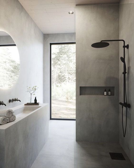 a minimalist grey bathroom clad with tiles and concrete, with a white concrete vanity and sink and black fixtures