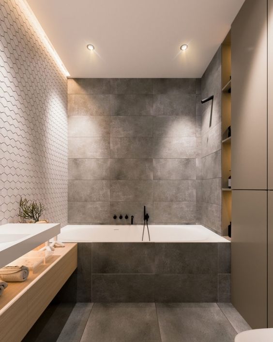 a minimalist grey bathroom done with tiles, with a large sleek storage unit and a wooden vanity plus built-in lights