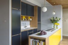 a minimalist kitchen done in navy and bright yellow, with natural wood touches and pendant lamps