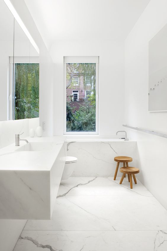 a-minimalist-white-bathroom-done-with-marble-a-floating-sink-and-marble-clad-tub-plus-a-window.jpg