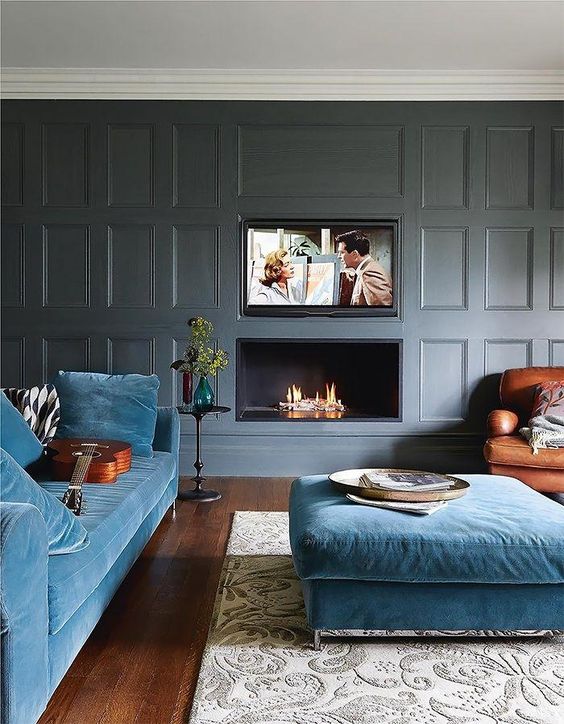 a modern luxurious living room with grey paneled walls, blue furniture and a built-in fireplace and TV