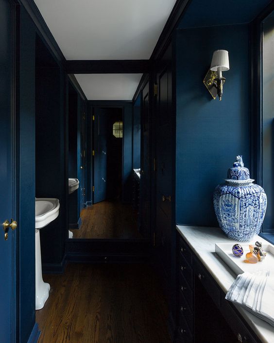 a moody navy powder room with all-navy walls, chic gold fixtures and lamps and white stone touches here and there