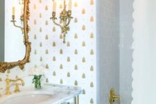 a refined bathroom with white and gold pineapple wallpaper, godl fixtures, a vanity and an exquisite mirror in a gold frame