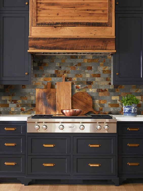 a retro navy kitchen with a wooden hood, gold handles and a gey and brown backsplash of gorgeous tiles