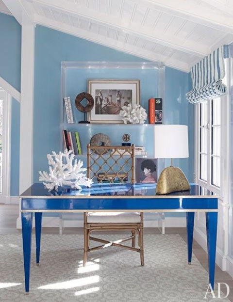 a seaside blue home office with light blue walls, a bright blue desk, an acrylic shelf and corals for a coastal feel